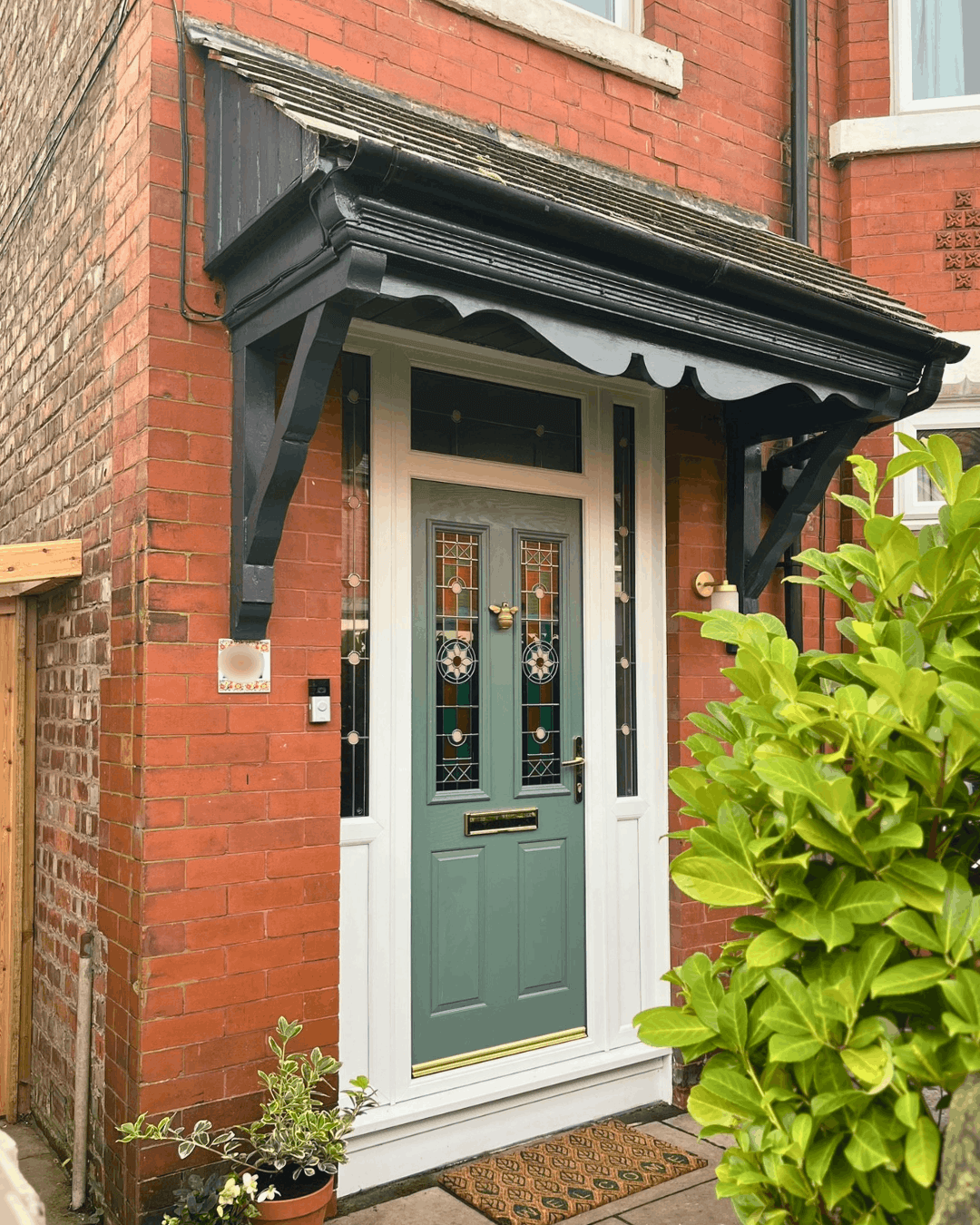 Green Victorian front door with stained glass panels, black canopy porch and plants at entrance