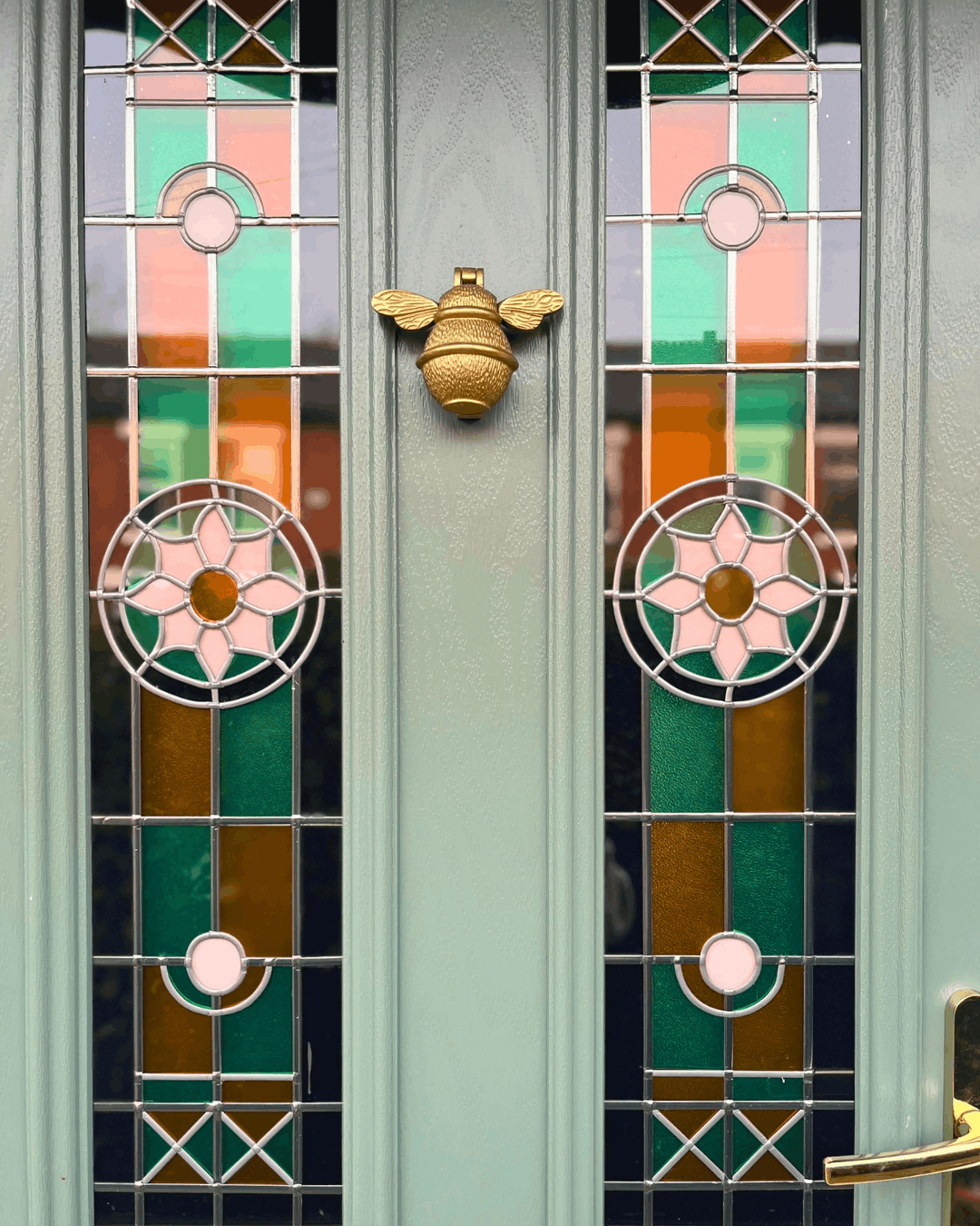 Close-up of sage green front door with stained glass detailing and brass bee door knocker